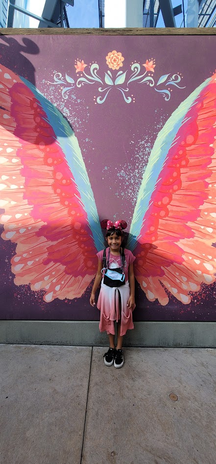 Photo of Mia standing in front of mural of wings
